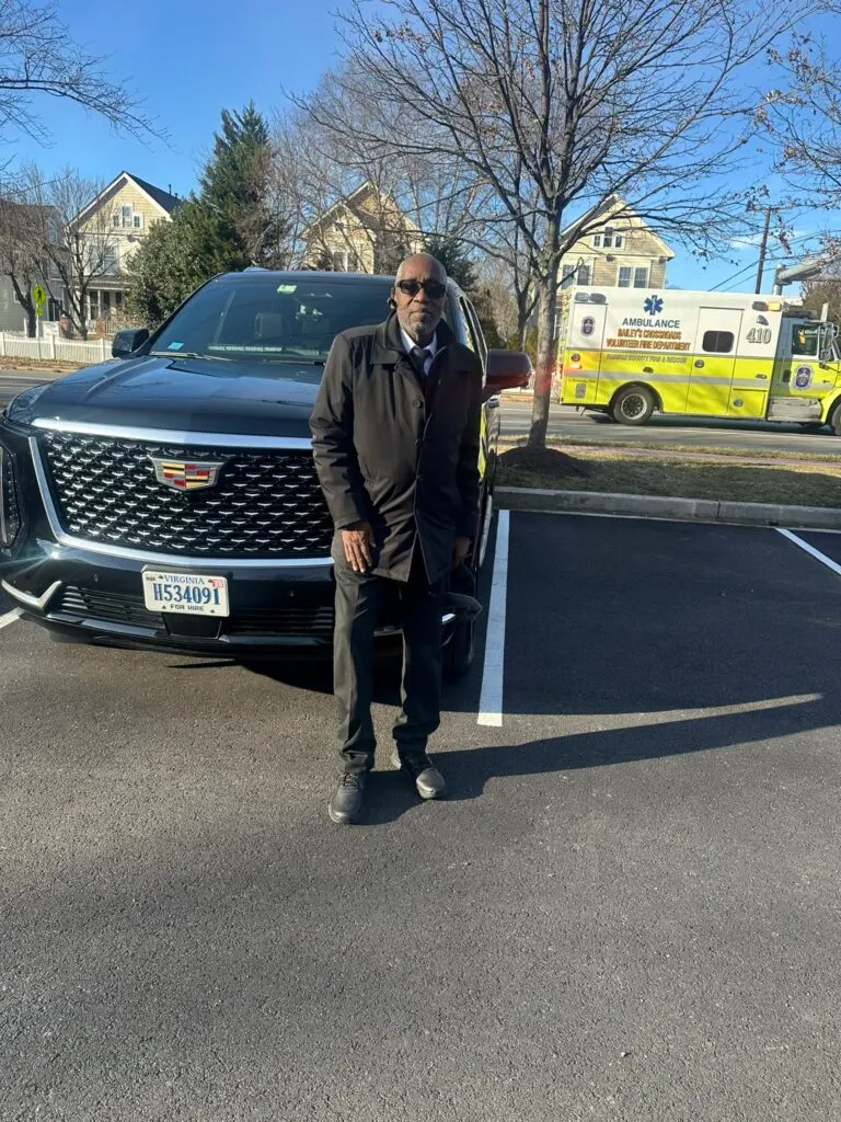 Uniformed chauffeur standing beside a black Cadillac Escalade